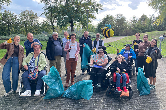 Gruppenfoto mit ca. 20 Menschen, vier davon in Rollstühlen, ausgestattet mit Müllsäcken, Müllgreifern und Handschuhen