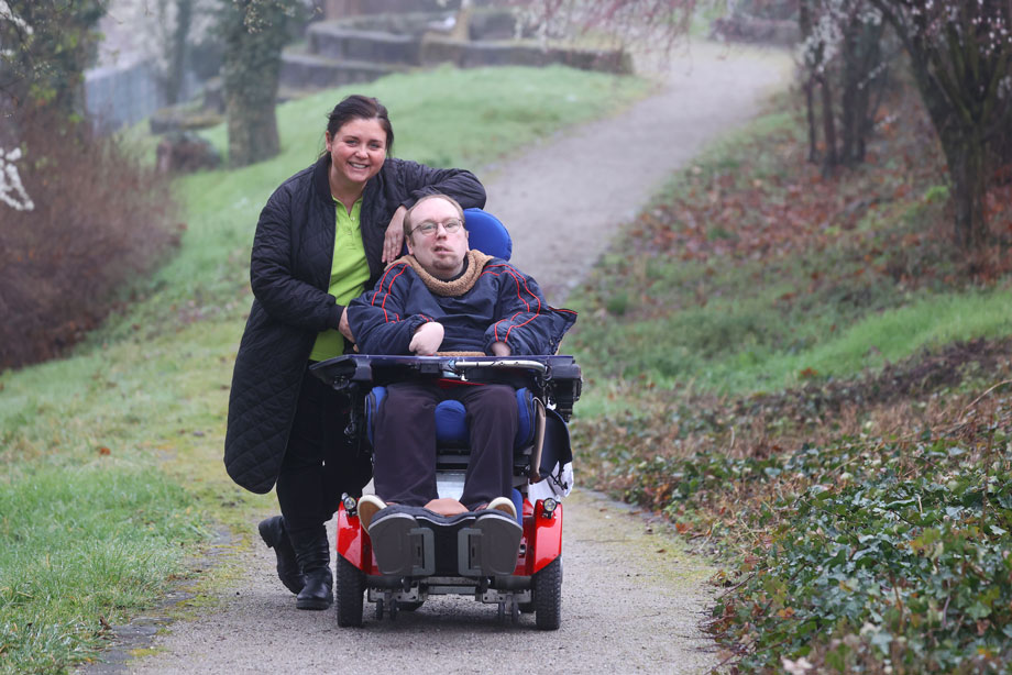 Spaziergang: Eine Person schiebt eine andere Person in einem Rollstuhl.